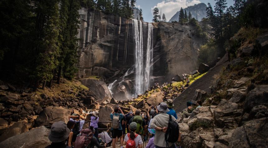 Foreign tourists standing at the entrance of a US national park with landscape view, representing new increased entry fees for international visitors from 2026.